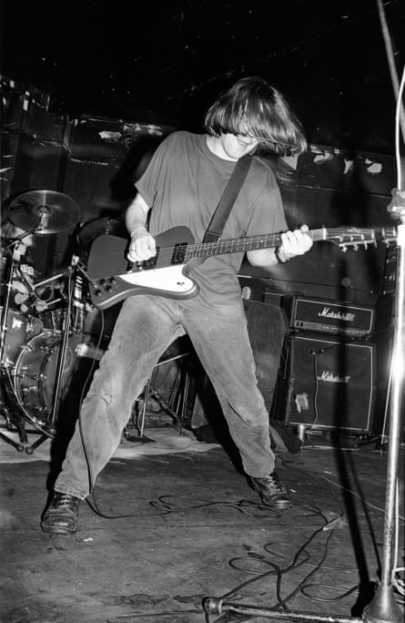 A black and white image of Norman Blake with long hair covering his face, playing guitar on stage in 1992.