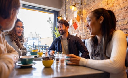 Four friends laugh and smile while having coffee in a cafe