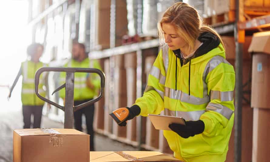 a warehouse worker stands amongst the aisles and scans stock with her hand scanner .