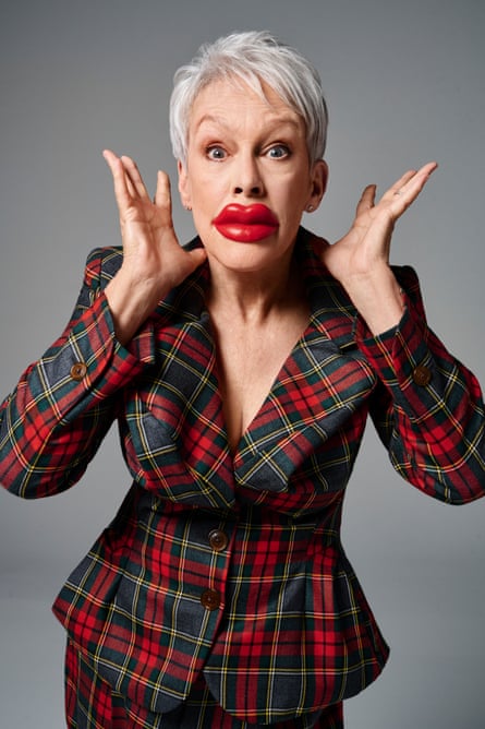 Portrait of Jamie Lee Curtis wearing big plastic red lips and a tartan suit with her hands on either side of her face