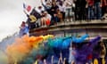 People climb on a vandalized building in France at a protest, with rainbow-colored powder flying through the air