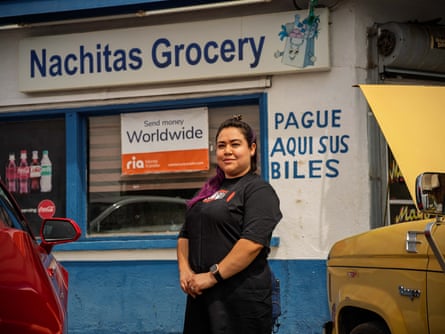 A business owner stands in front of her bright blue and white store with signs advertising bill payments in Spanish