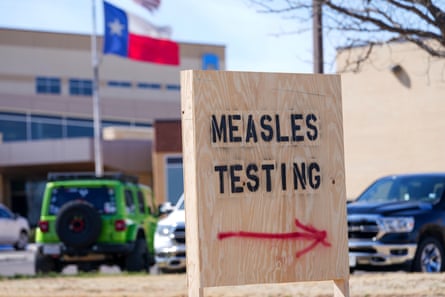 A stencilled wooden sign with an arrow spray-painted on it near a car park with the Texas flag seen in the background
