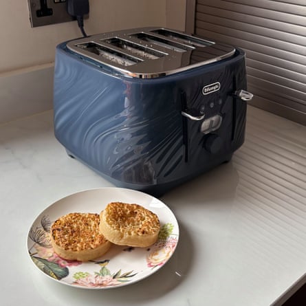 A blue DeLonghi Ballerina Seta 4 Slot Toaster on a worktop next to a plate with two crumpets on top