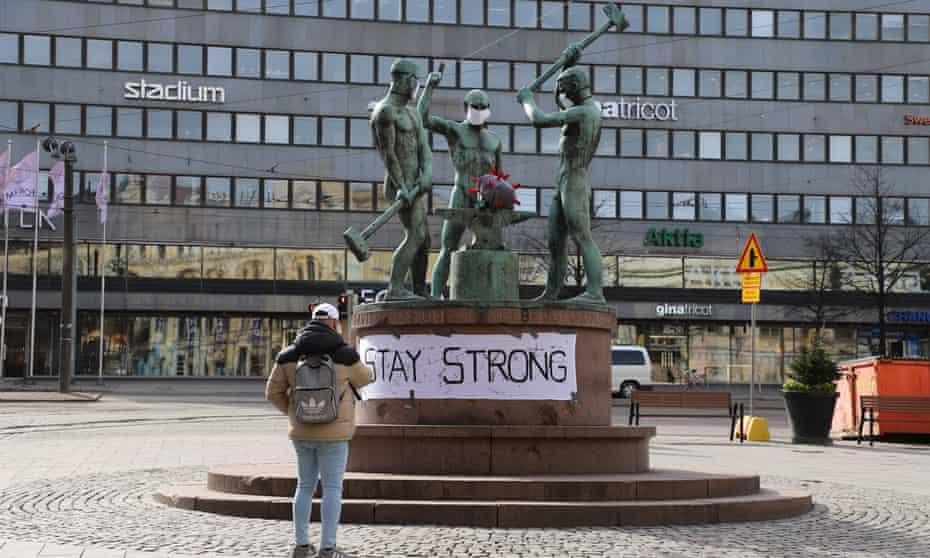 A man  takes a picture of the famous city sculpture Three Smiths, which have facial masks, in Helsinki, Finland