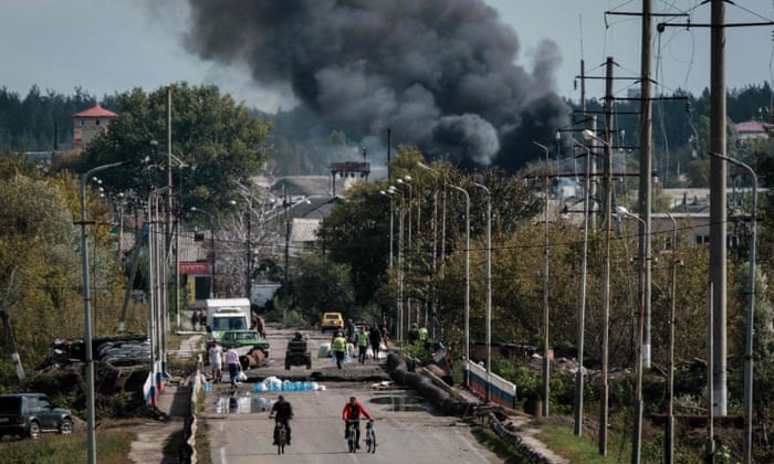 People cross a bridge over the Oskil River as black smoke rises in the frontline city of Kupiansk, Kharkiv region.