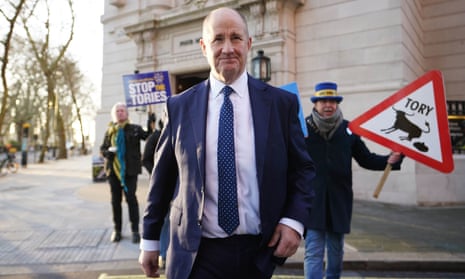 Kevin Hollinrake walking in London with activists holding anti-Tory placards behind him