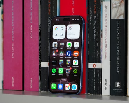 The iPhone 18 Pro leaning against some books showing a home screen full of app icons