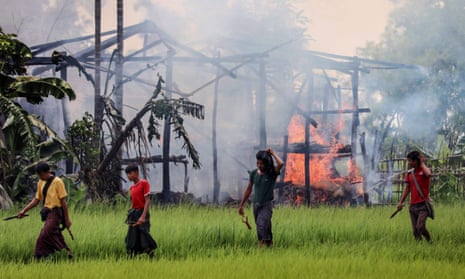 Unidentified men carry knives and slingshots as they walk past a burning house in Gawdu Tharya village near Maungdaw in Rakhine state, northern Myanmar