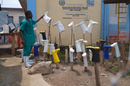 A health worker holds a white boot by the sole next to other upturned boots on poles and rods