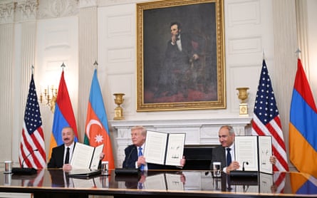 The presidents of Azerbaijan and the United States, along with the prime minister of Armenia sit on one side of a long table in the White House, each holding a signed document in front of the national flags of their countries