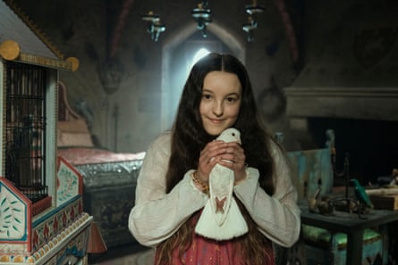 Bella Ramsey wearing a red dress and white cardigan, holding a white bird in front of her with both of her hands wrapped around it