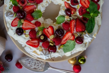 Close-up of a pavlova wreath decorated with strawberries, raspberries, cherries, and mint leaves.