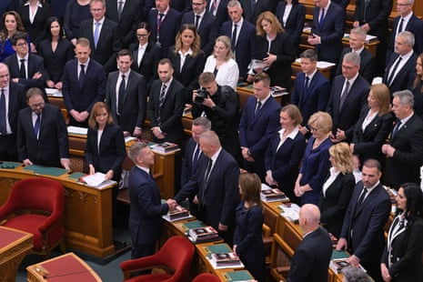 Péter Magyar shakes the hand of a minister-elect in parliament as everyone looks toward him walking up the aisle.