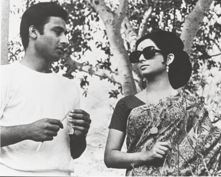 Black and white photo of an Indian man in a T-shirt looking at an Indian woman with sunglasses and wearing a sari in front of a tree