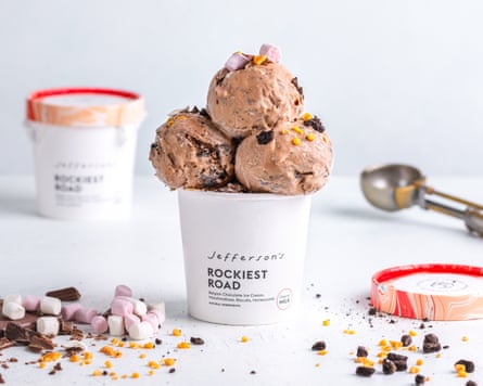 A tub on Rockiest road ice-cream with three scoops on top, an ice-cream scoop and ingredients scattered over a counter top