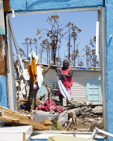 a woman in a pink shirt hangs up clothes on a tree, surrounded by debris