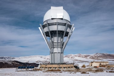A tall grey pavilion with white dome on top in a snowy landscape