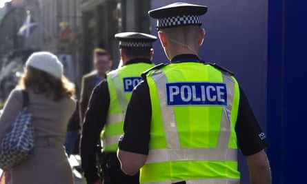 Two police officers walk away from camera down a street; they wear yellow hi-vis vests and appear to be on a patrol