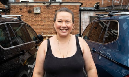Lauren Cakalli, wearing black vest top and smiling as she stands between two cars