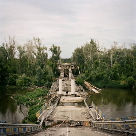 A destroyed bridge that has fallen into a river with trees along its bank