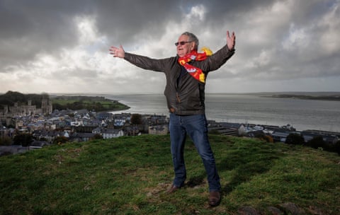 Dafydd Iwan, wearing a Wales scarf embroided with the words of his famous song Yma o Hyd, stands on Twthill overlooking Caernarfon Castle.