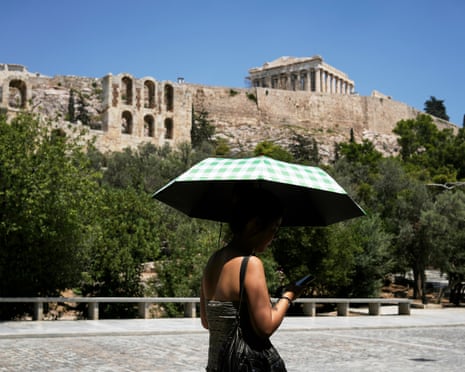 A tourist holding an umbrella against the sun passes by the Acropolis hill which remained closed for five hours due the new heatwave in Athens, Greece.