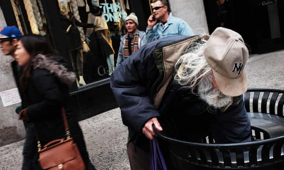 A homeless man looks for food in a litter bin on a retail street in New York.