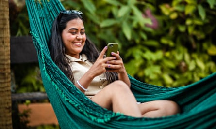 Smiling woman in hammock using mobile phone outside on a patio