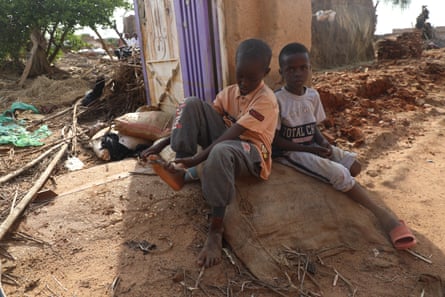 Two young boys sit by a damaged house