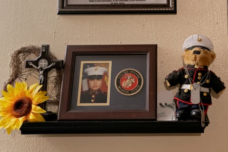 a detail image of a shelf adorned with a framed image of a woman in military uniform, a cross, a sunflower, and a stuffed animal.