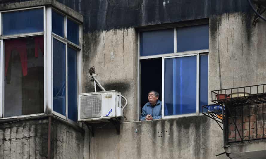 A man looks out of the window at a residential compound in Wuhan