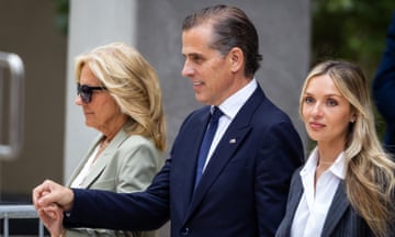 Two white women and one white man in a row, all smiling although a bit grimly, with the man in the middle holding the man of the older woman to his right. Both of the women have long blond hair.
