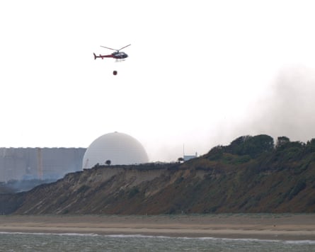 A helicopter trailing a water bucket below flies past Sizewell B nuclear power station