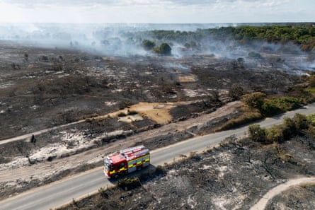 Fire engine driving along a road past a burned forest with smoke rising in the background