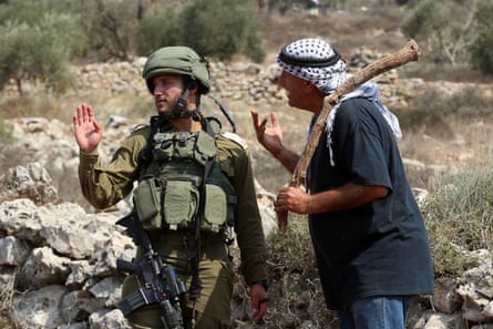 An Israeli soldier with a Palestinian farmer who is waiting to reach a farm to harvest olives, in Yetma, the West Bank.