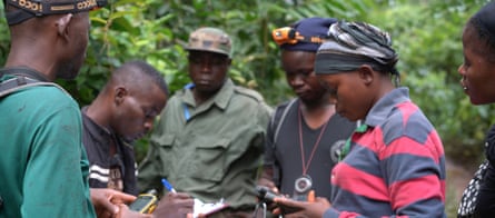 A group of men and women take notes at a briefing in a forest.
