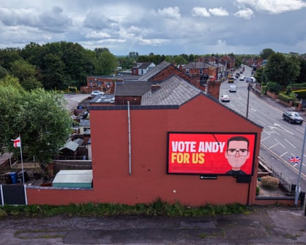A video screen on the side of the house with a cartoon of Andy Burnham's face and the words "Vote Andy for us"