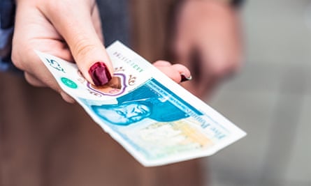 Close-up of a woman paying with a Bank of England five pound note, the first English note made of polymer plastic.