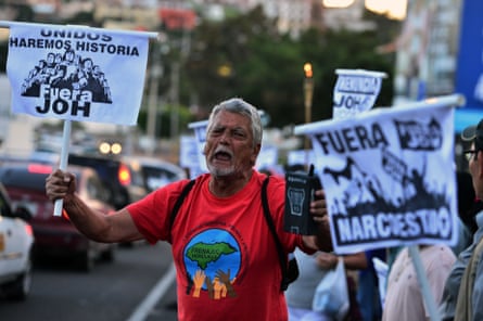 An opposition supporter holds signs reading ‘Together we will make history. JOH out’ and ‘Narco-state out’ as he demonstrates against President Juan Orlando Hernández in Tegucigalpa