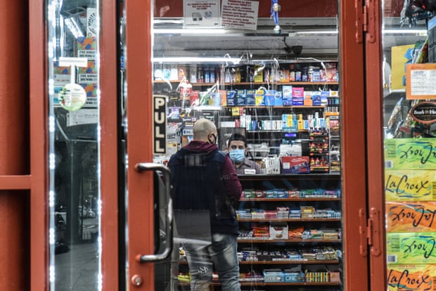 A photo taken through the doorway of a bodega shows a man standing at the counter while another behind the counter wears a mask.