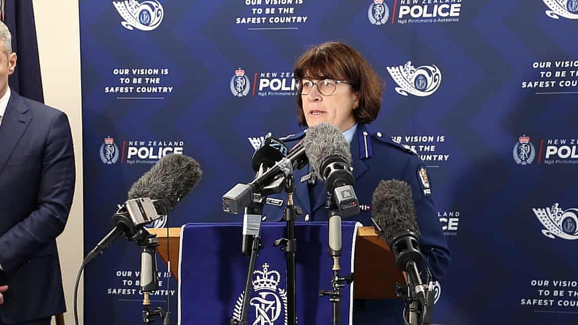 A New Zealand police office speaks at a lectern in front of numerous microphones