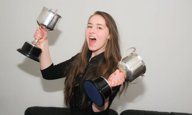 Young teenage girl holding silver cups school trophies.