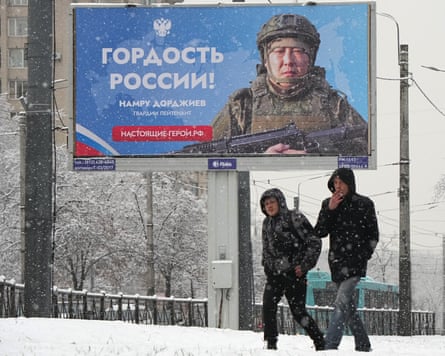 Men walk past a billboard with an image of a Russian soldier