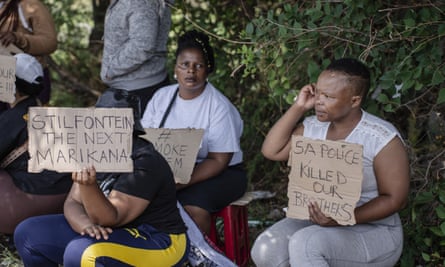 Women hold signs reading ‘SA police killed our brothers’