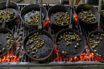 snails being cooked in dry frying pans over a charcoal grill