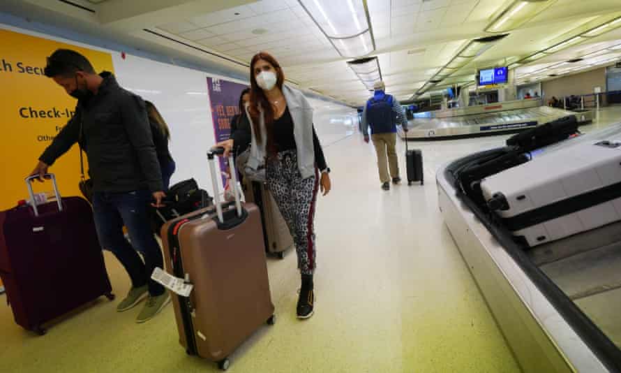 Los viajeros usan cobertores faciales mientras transportan equipaje desde un carrusel en la terminal principal del aeropuerto internacional de Denver.