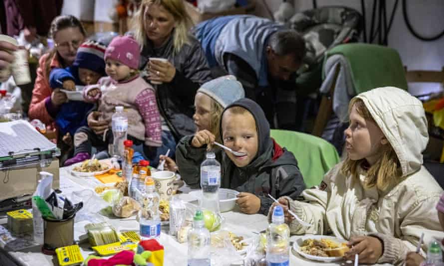 Mężczyźni, kobiety i dzieci jedzący i pijący w namiocie spożywczym w Zaporożu, aby podawać jedzenie ewakuowanym po przybyciu z Mariupola