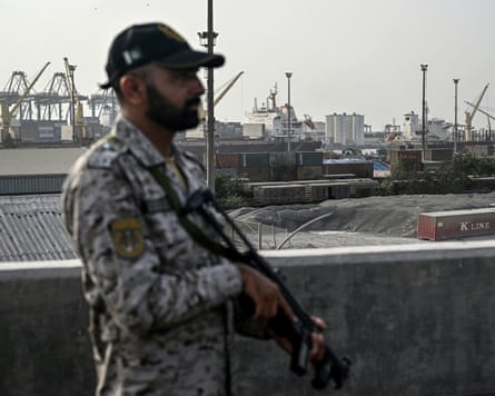 An armed security officer stands guard with port cranes in the background