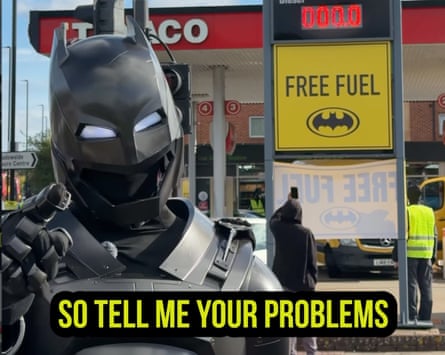 ‘London’s Batman’ poses in costume beside a petrol station sign reading ‘Free Fuel’